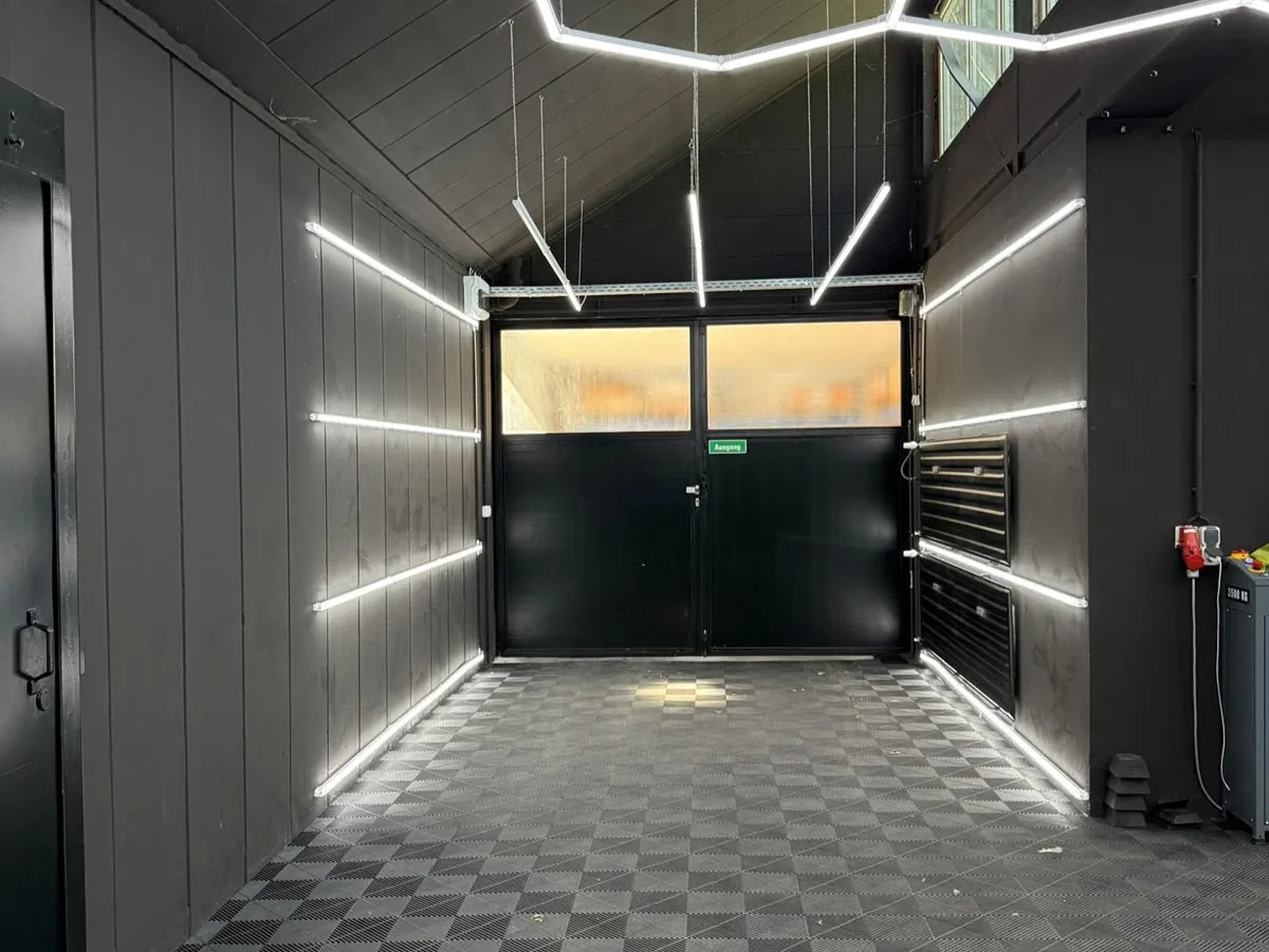 Dieselbe Werkstatthalle nach dem Ausbau durch COLORD Meisterbetrieb, dunkle Wandverkleidung, LED-Lichtlinien und neuer Bodenbelag